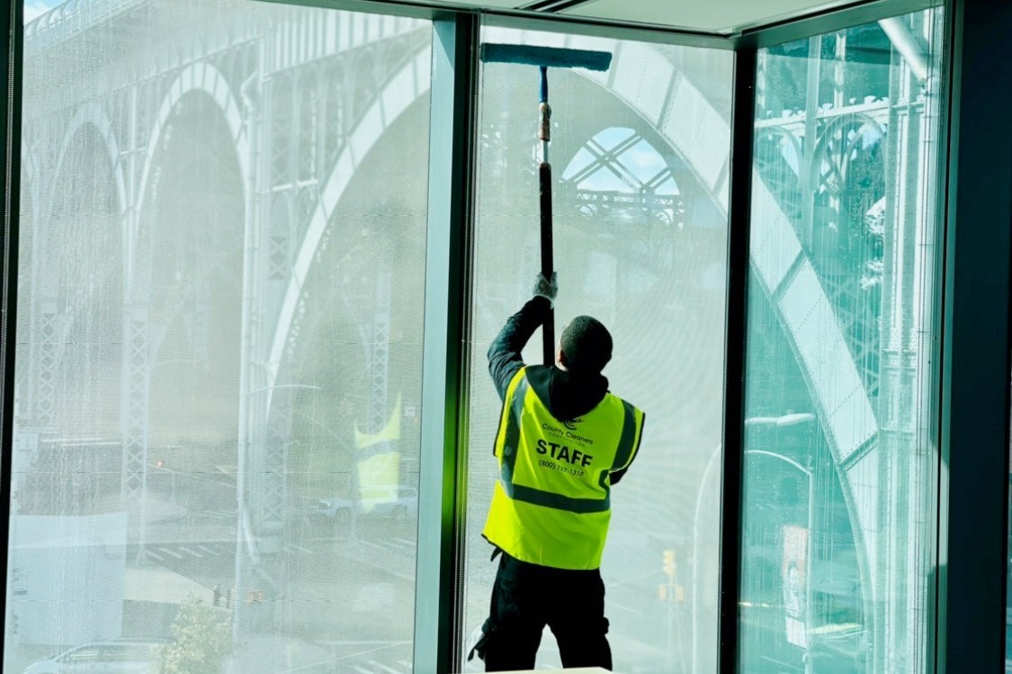 A window cleaner is cleaning a very tall window of a building, with the Viaduct in the background.