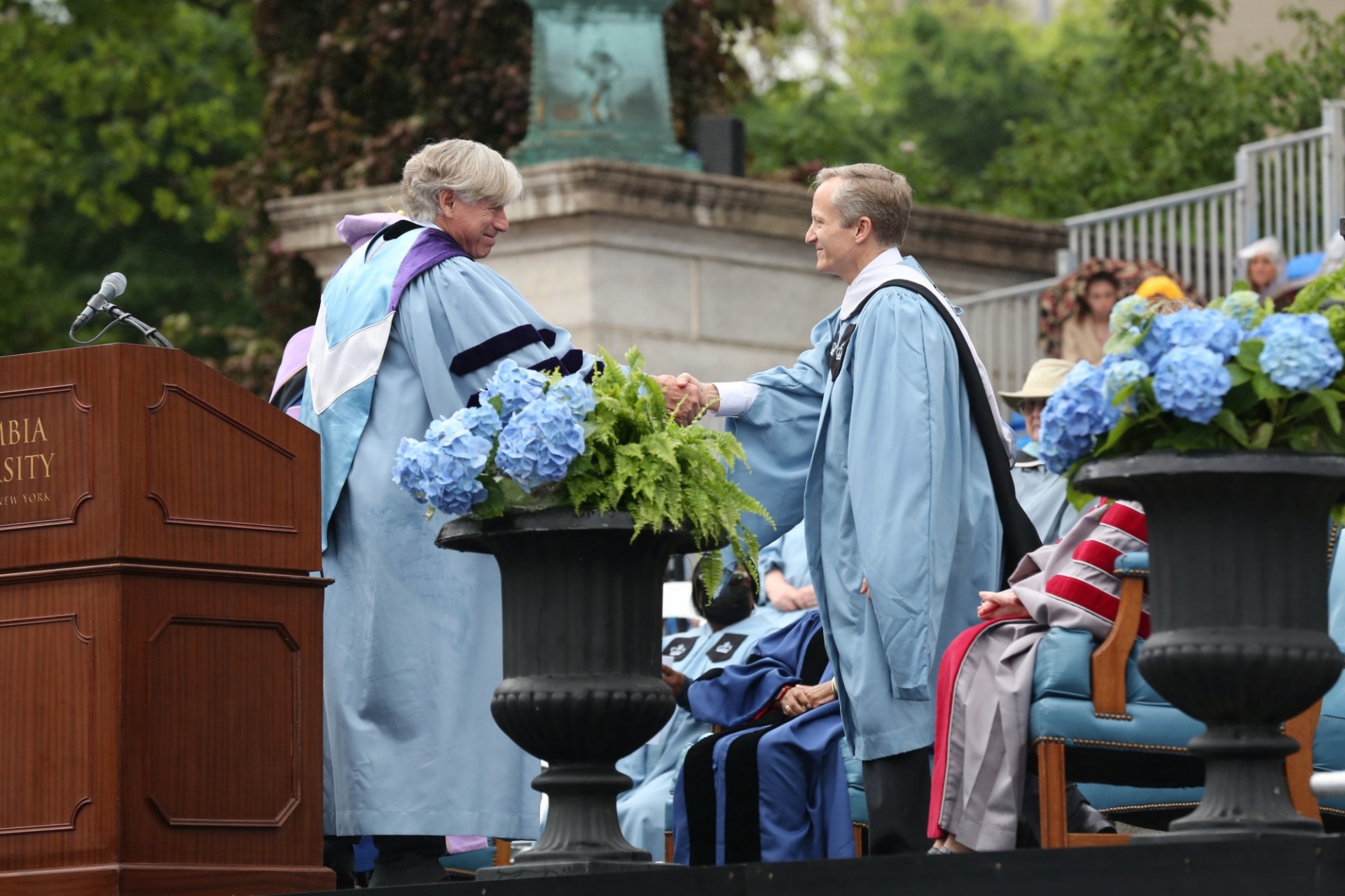 IPresident Bollinger shakes David M. Greenberg's hand during Commencement.  Both are wearing Commencement regalia.  