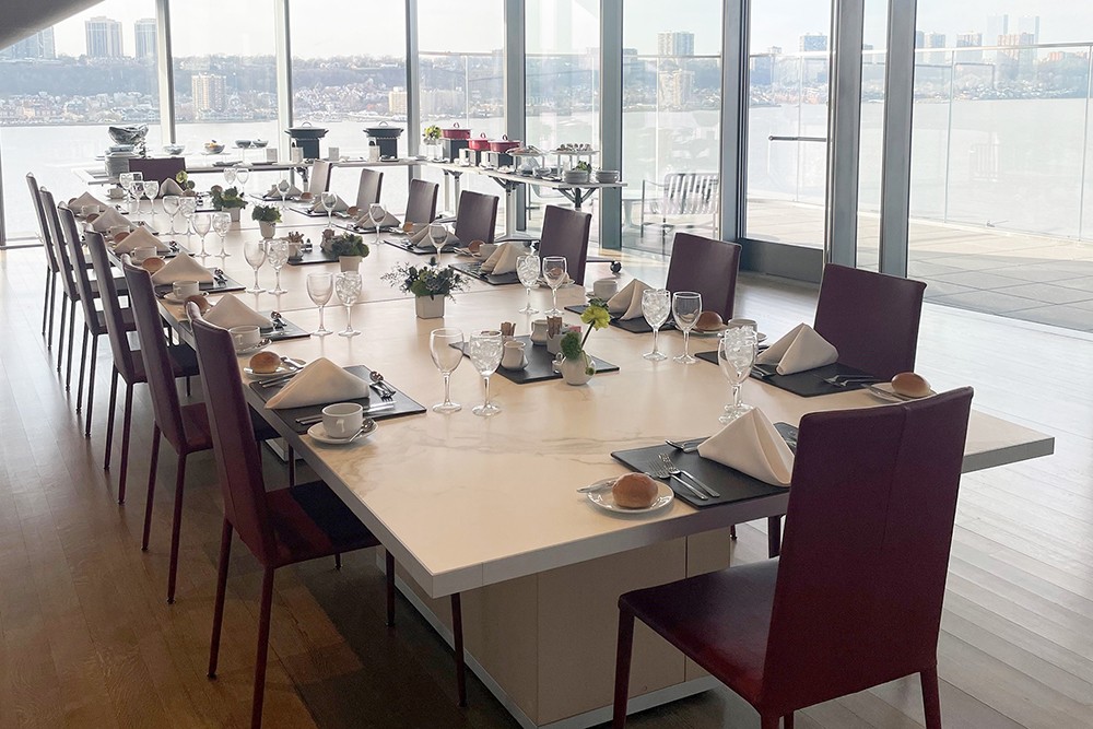 A long table is set up for a catered lunch in an event space in Henry R. Kravis Hall, which overlooks the Hudson River.