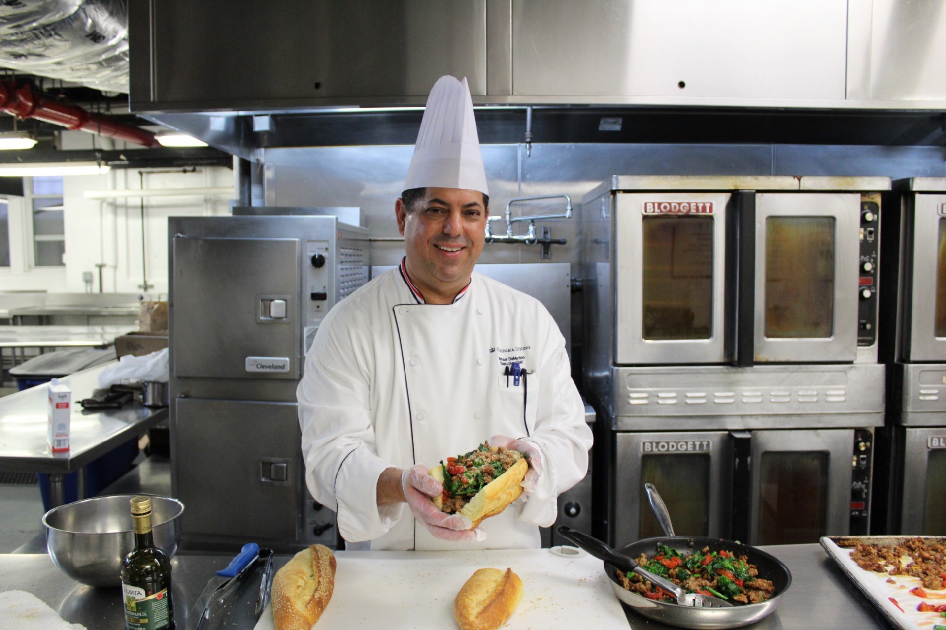 Chef Mike is in a kitchen, holding up the Grandma sub that he just prepared.