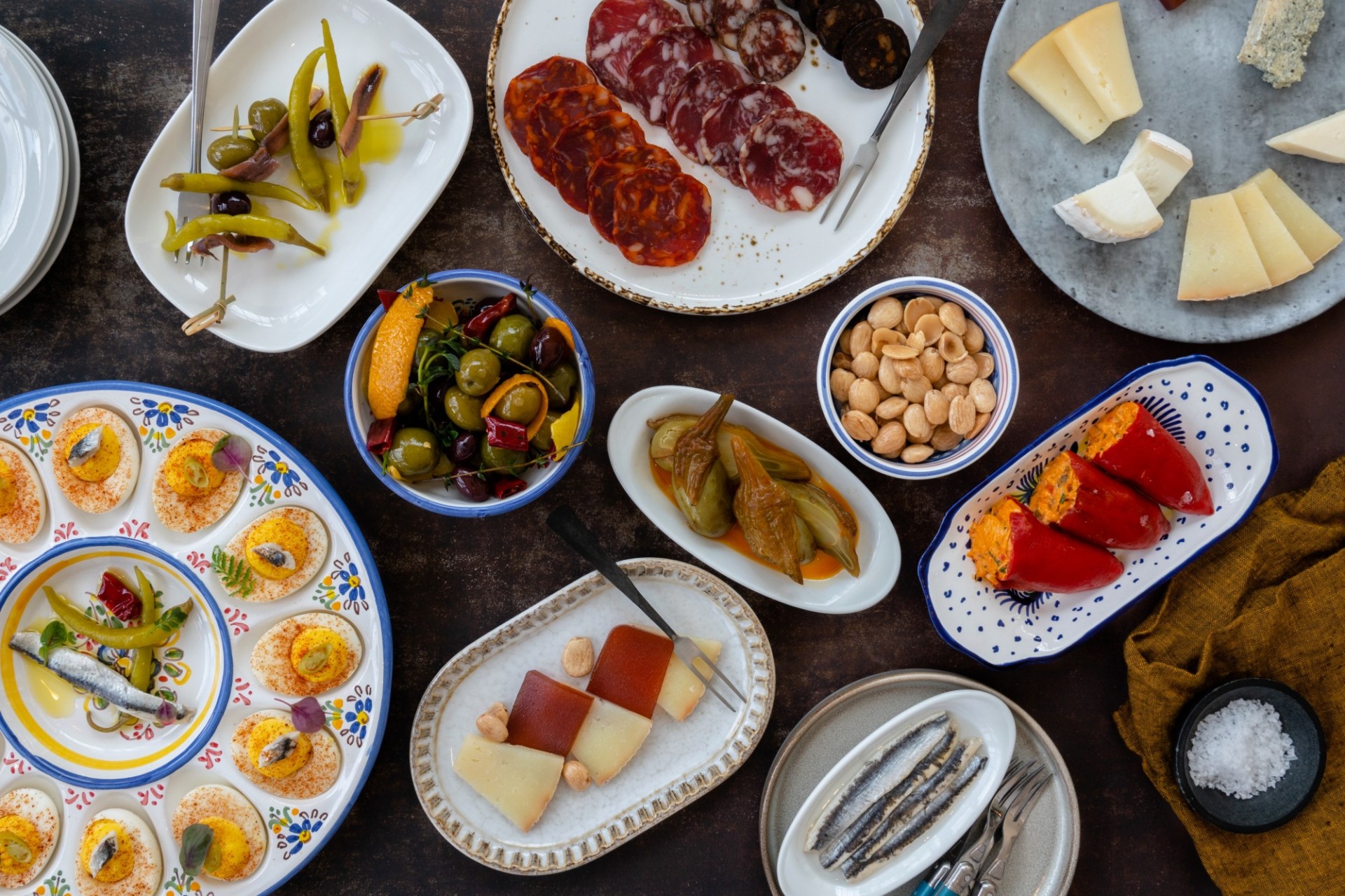 A selection of tapas plates, including peppers, cheese, deviled eggs, and meats.