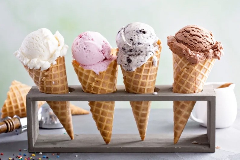 Four ice cream cones with vanilla, strawberry, cookies and cream, and chocolate, respectively sit in a cone container.  
