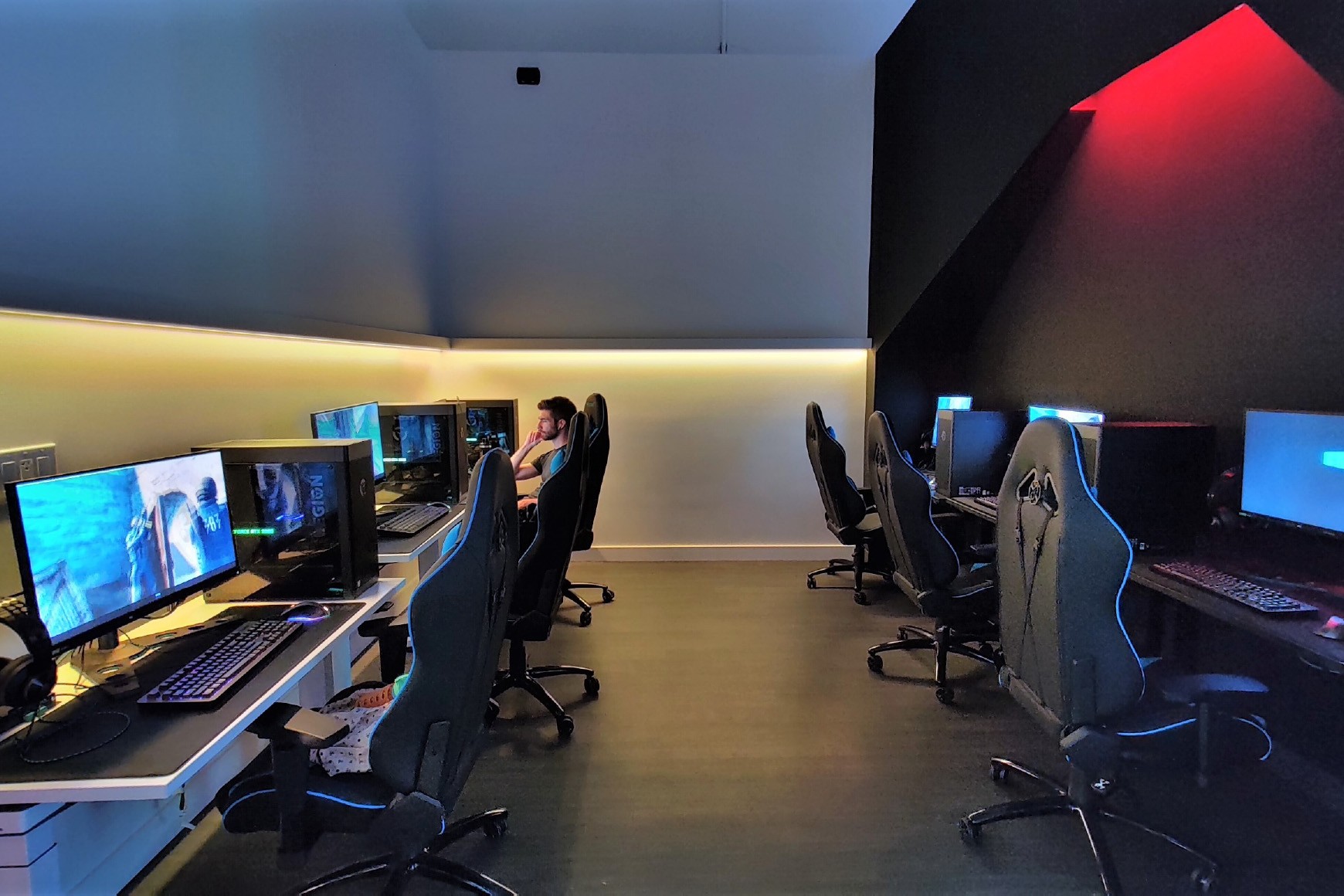 Two rows of gaming computers are set up against opposite walls, with ambient lighting throughout