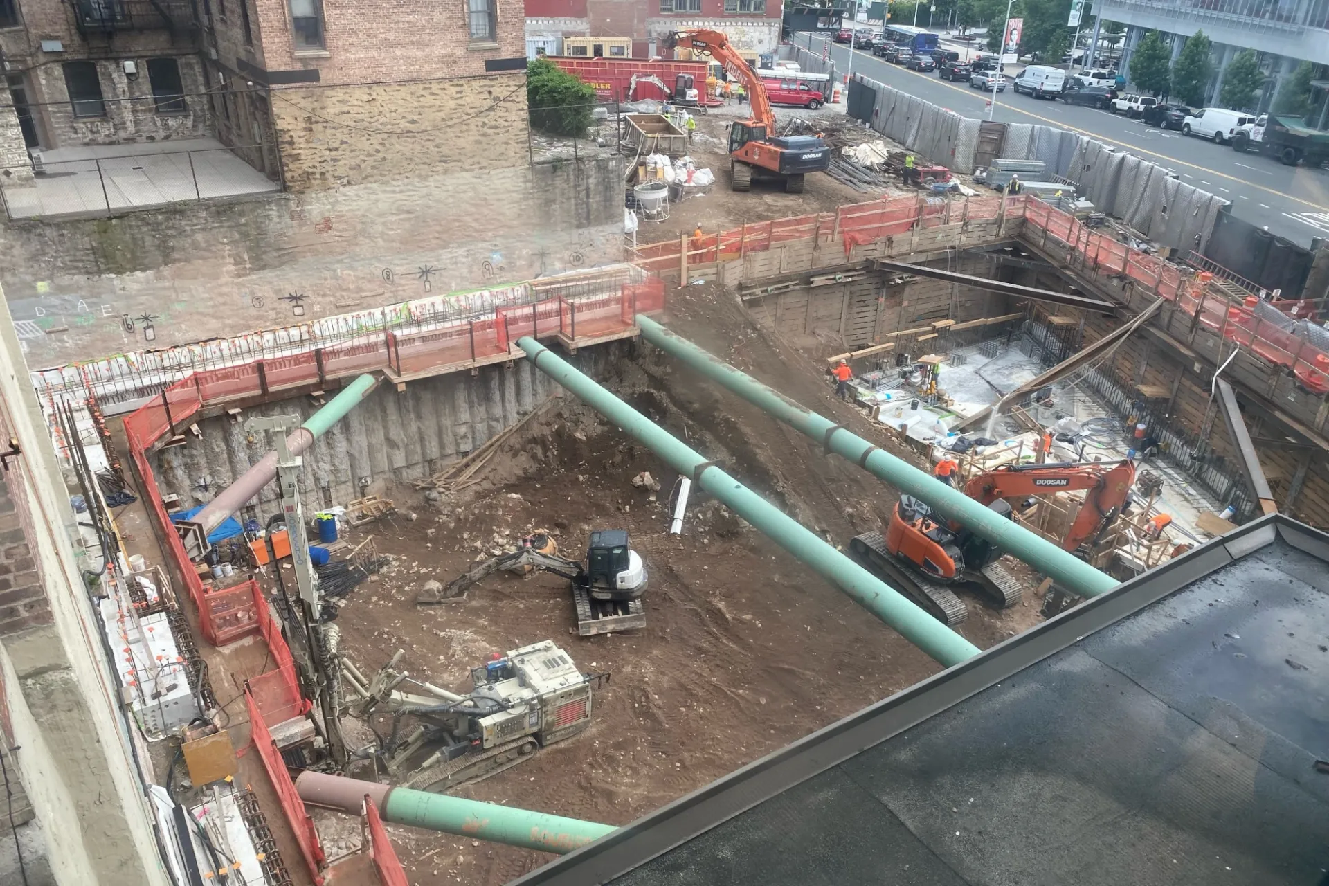 An excavated pit with large green pipes running overhead at the 600 W. 125th Street construction site.