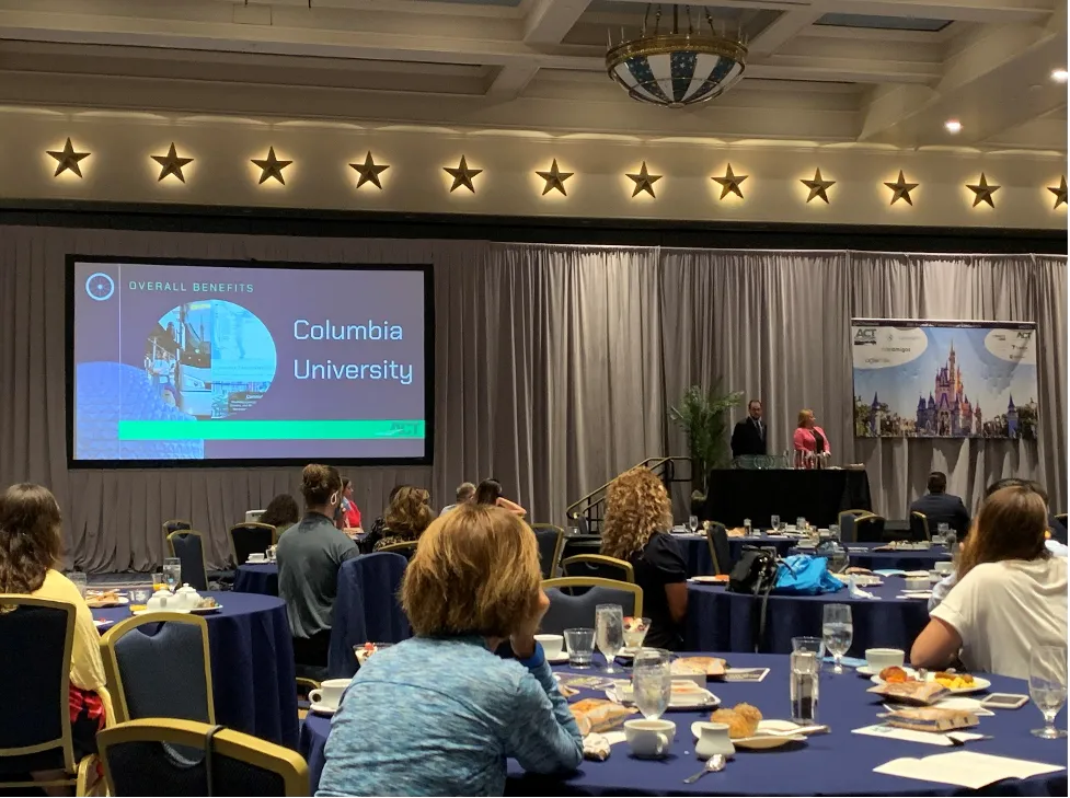 A group of people sitting in a banquet hall with a slide recognizing Columbia University for its overall transportation benefits on the stage.