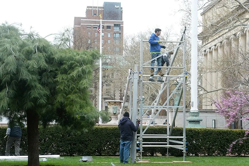 Workers are on scaffolding setting up the bleachers for Low Plaza.