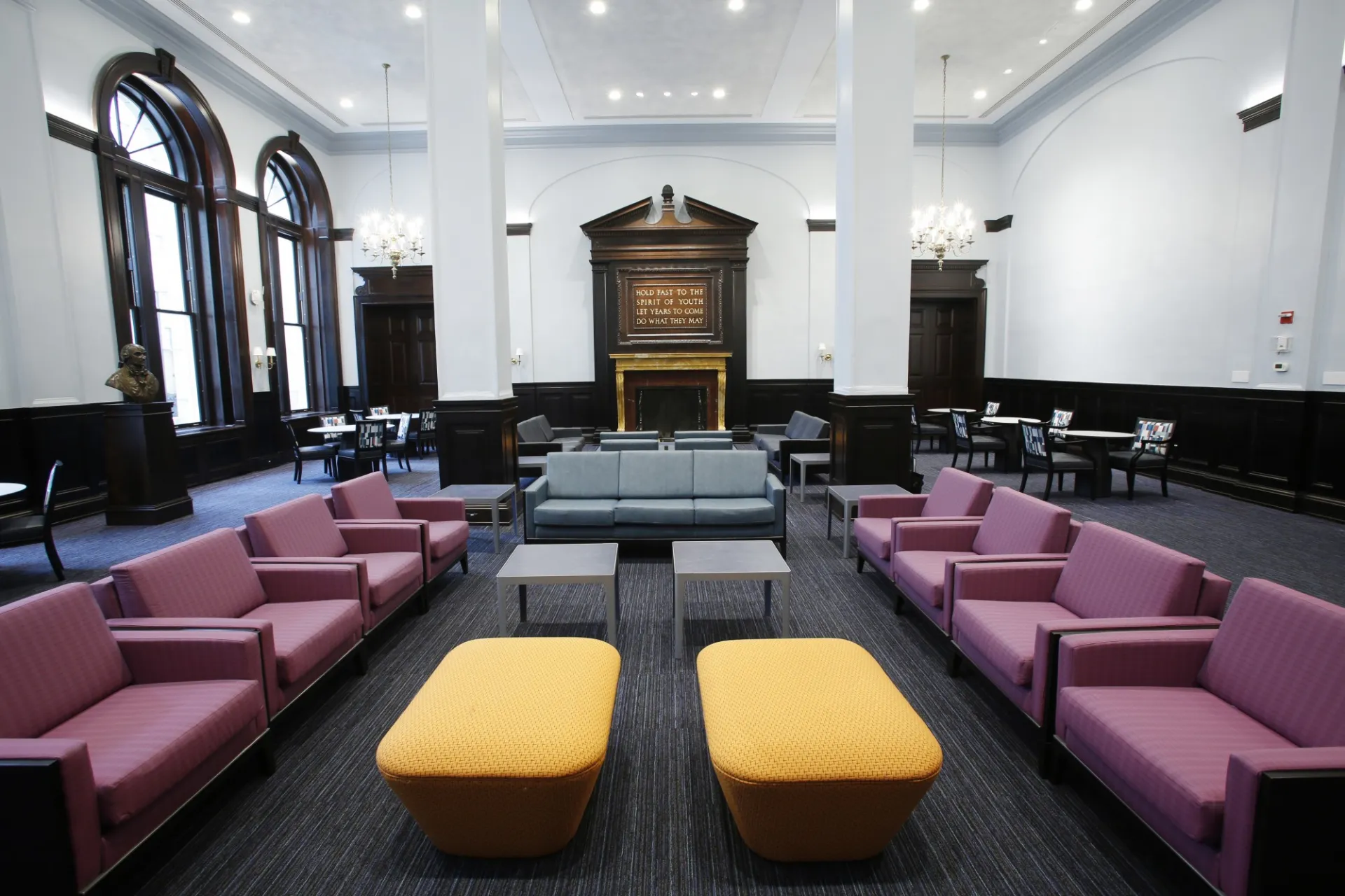 A view of the John Jay lounge, with bright, white walls, wooden accents, and mauve, gray, and mustard collar furniture.
