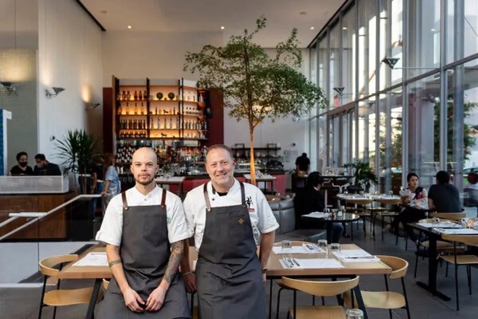 Chef Becker stands with another chef inside Oliva, which has a bar in the background.