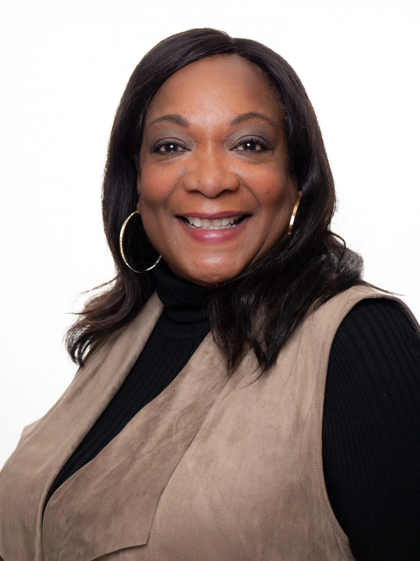 A headshot of Tanya Pope, who has medium length black hair and is wearing a tan vest over a black, long-sleeved shirt.